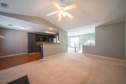 A spacious living room with a ceiling fan and a kitchen area in the background.