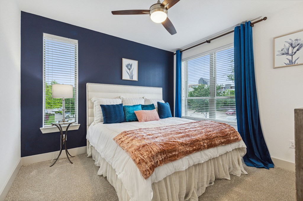 A bedroom with a bed, blue curtains, and a ceiling fan at Everra Midtown Park Apartments, Dallas, TX