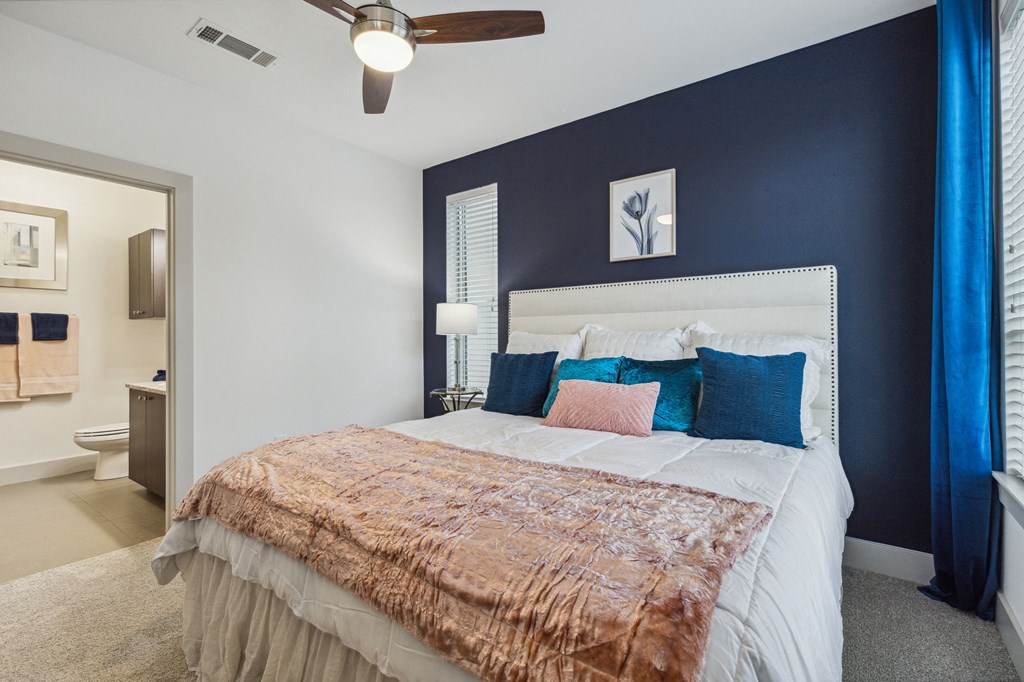 A bedroom with a bed, a ceiling fan, and a window with blue curtains at Everra Midtown Park Apartments, Dallas 75231
