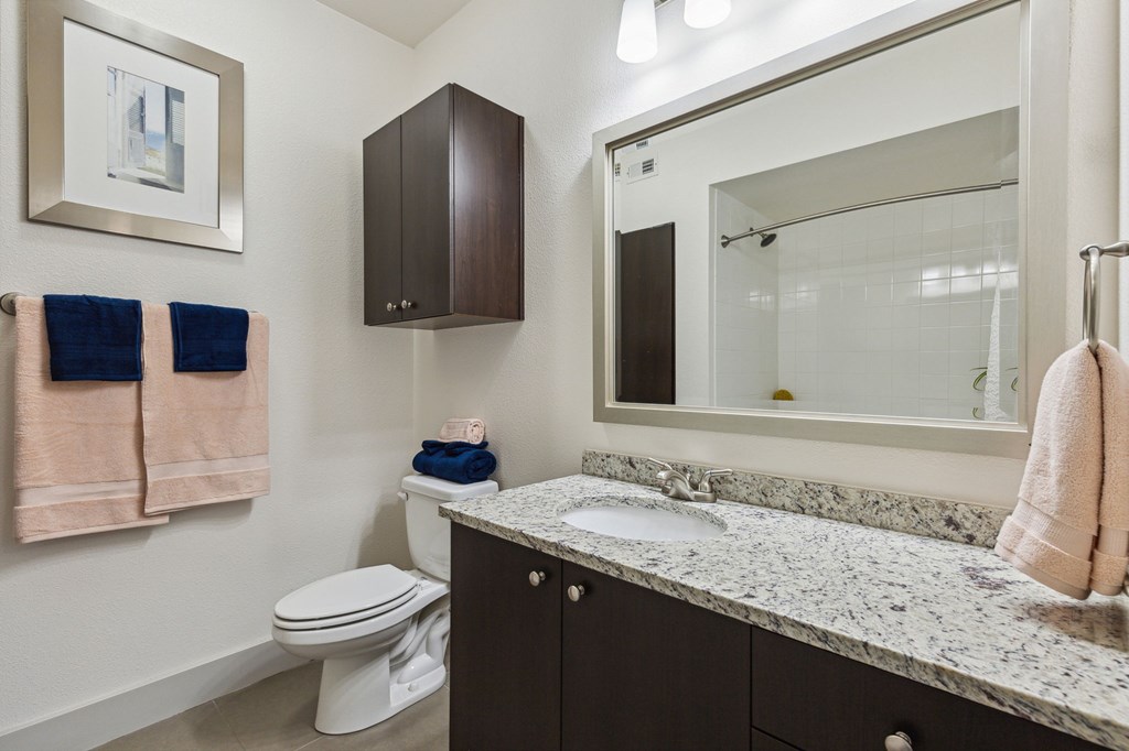 A bathroom with a toilet, sink, and towels at Everra Midtown Park Apartments, Dallas