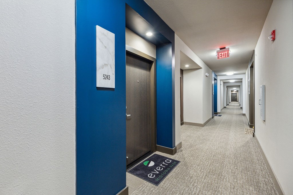 A hallway with a blue wall and a door with a sign that says 5245 on it at Everra Midtown Park Apartments, Dallas, TX