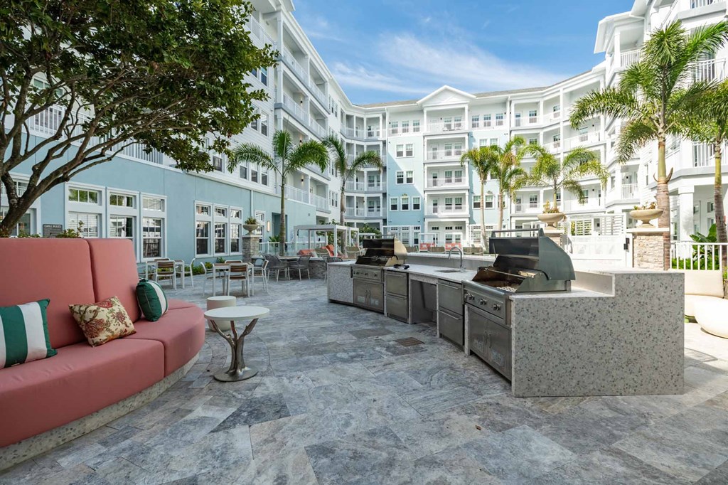 A pink couch sits in the middle of a courtyard with a grill and a table.