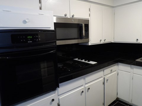 A black stove top oven sits next to a black microwave in a kitchen with white cabinets.