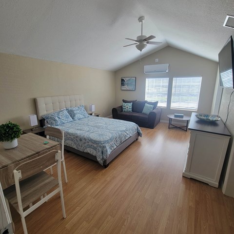 A bedroom with a bed, a chair, a table, and a ceiling fan.
