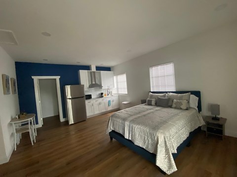 A bedroom with a bed, nightstand, and a kitchen area in the background.