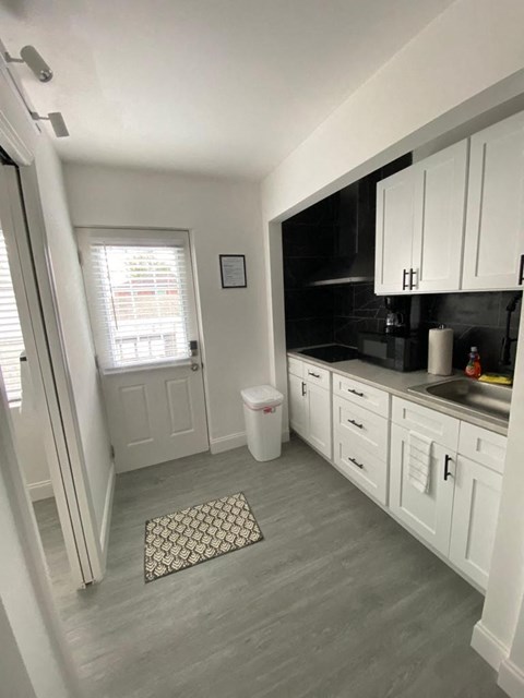 A kitchen with white cabinets and a window with blinds.