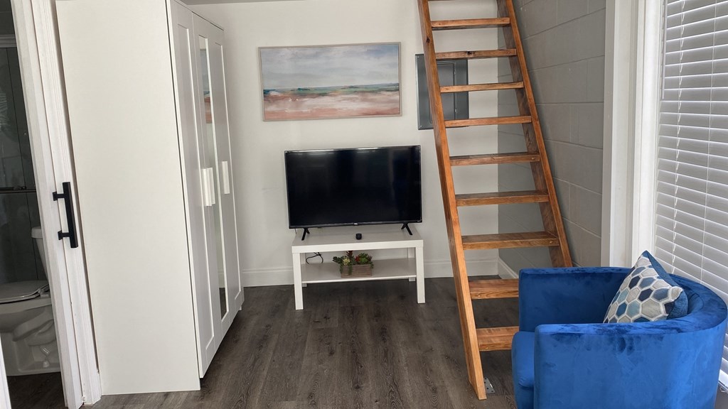 A blue chair sits in front of a television in a room with a painting on the wall and a wooden ladder.