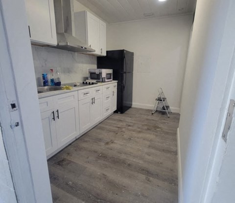 A kitchen with white cabinets and a black refrigerator.