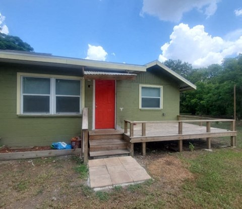 A green house with a red door and a wooden deck.