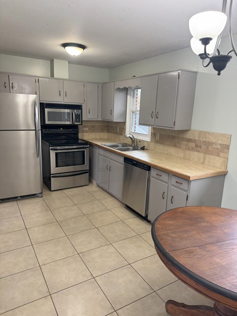 A kitchen with a refrigerator, oven, microwave, and sink.