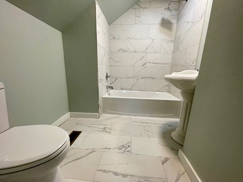 A white toilet is in a bathroom with marble tile flooring.