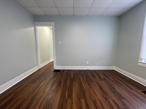 A room with wooden flooring and a doorway leading to another room.
