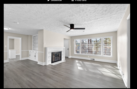 A spacious living room with a fireplace and a ceiling fan.