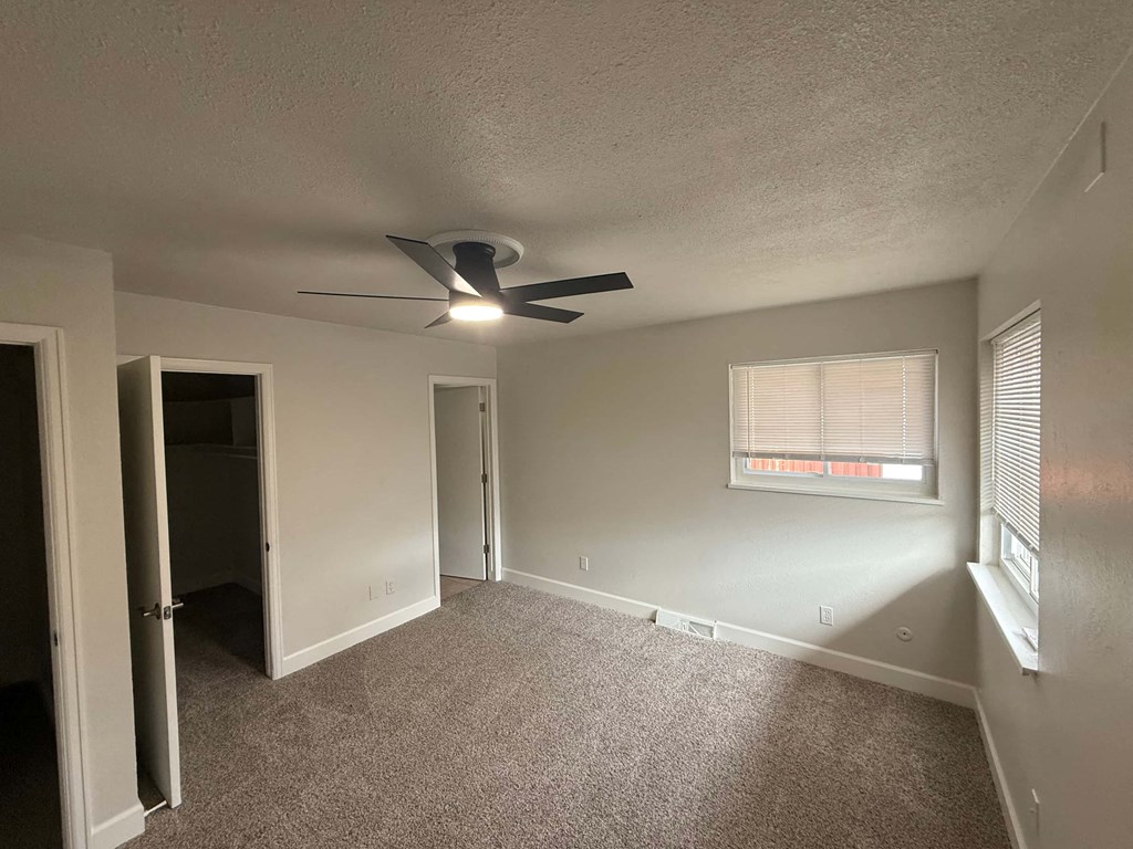 A room with a ceiling fan and a window with blinds.