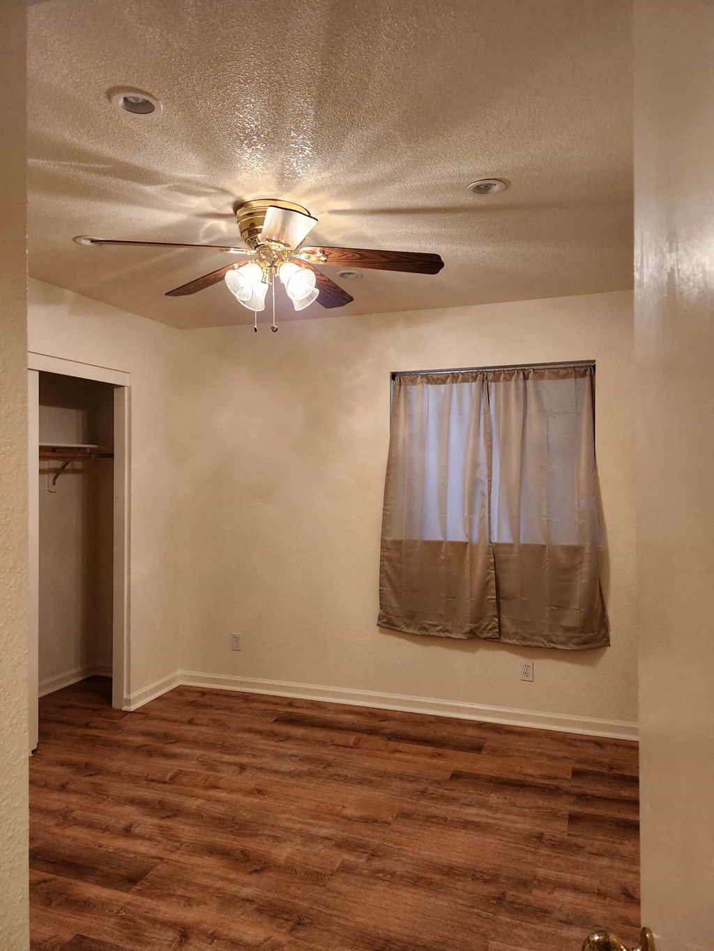 A room with a ceiling fan and a window with curtains.
