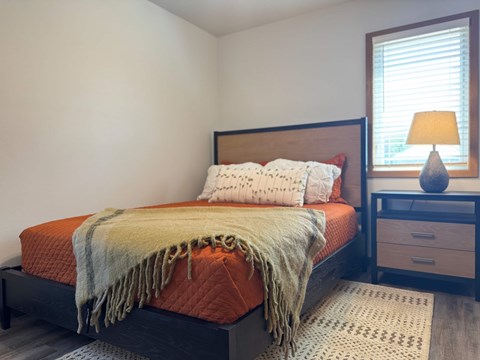 A bedroom with a bed, nightstand, and window.
