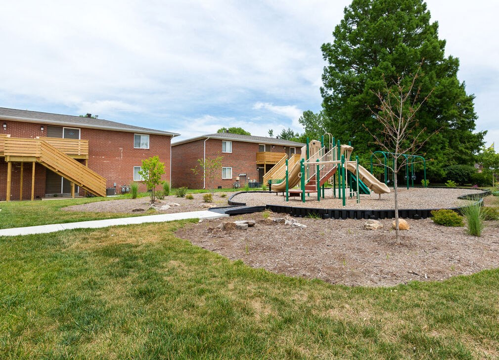 A playground with a green slide and a tree in the foreground.
