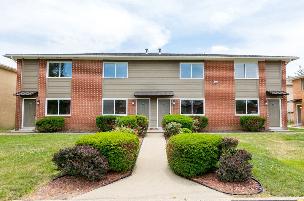 A building with a grey roof and a brick facade with a green bush in front.