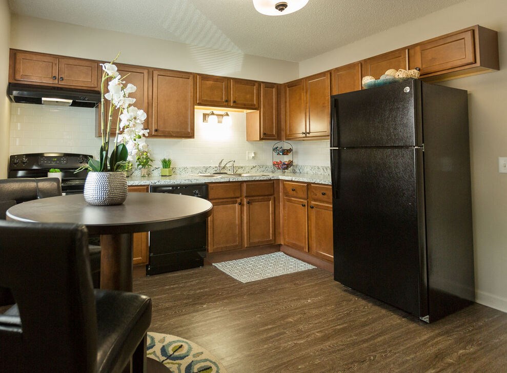 A black refrigerator stands in a kitchen with wooden cabinets and a round table.