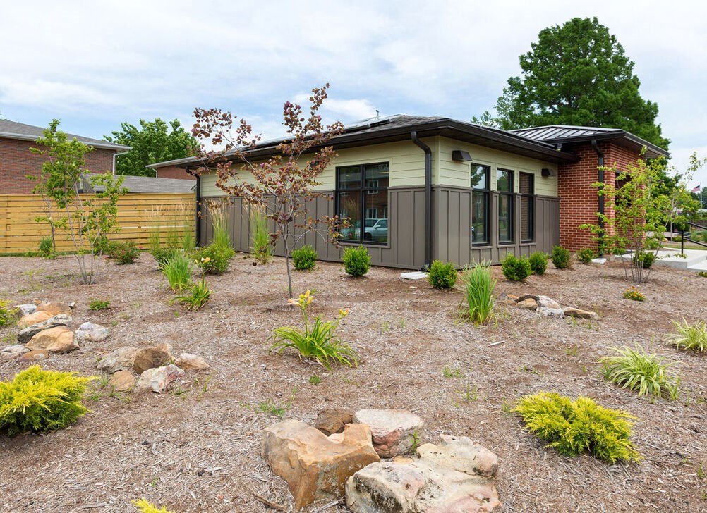 A house with a brown and beige exterior is surrounded by a garden with rocks and plants.