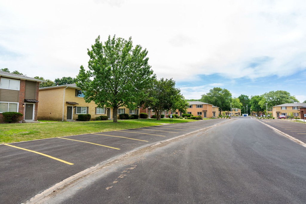 A parking lot with a tree in the middle and apartment buildings in the background.
