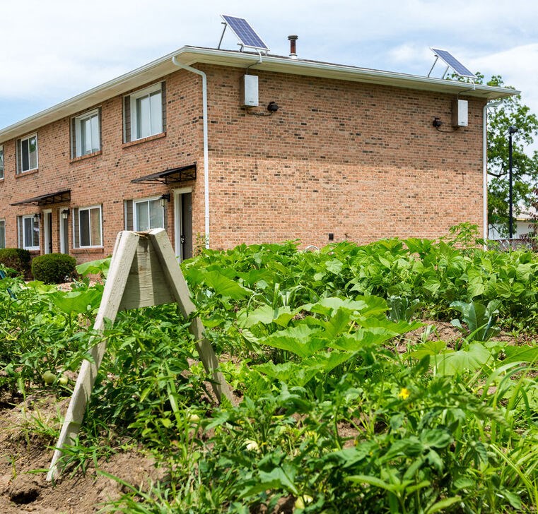 A brick house with a solar panel on the roof and a garden in front.