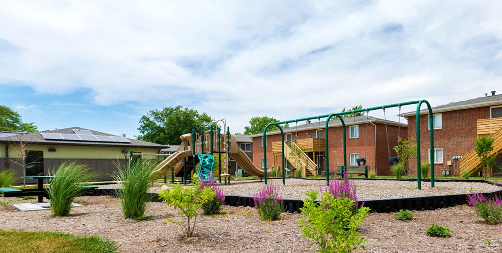 A playground with a green slide and a building in the background.