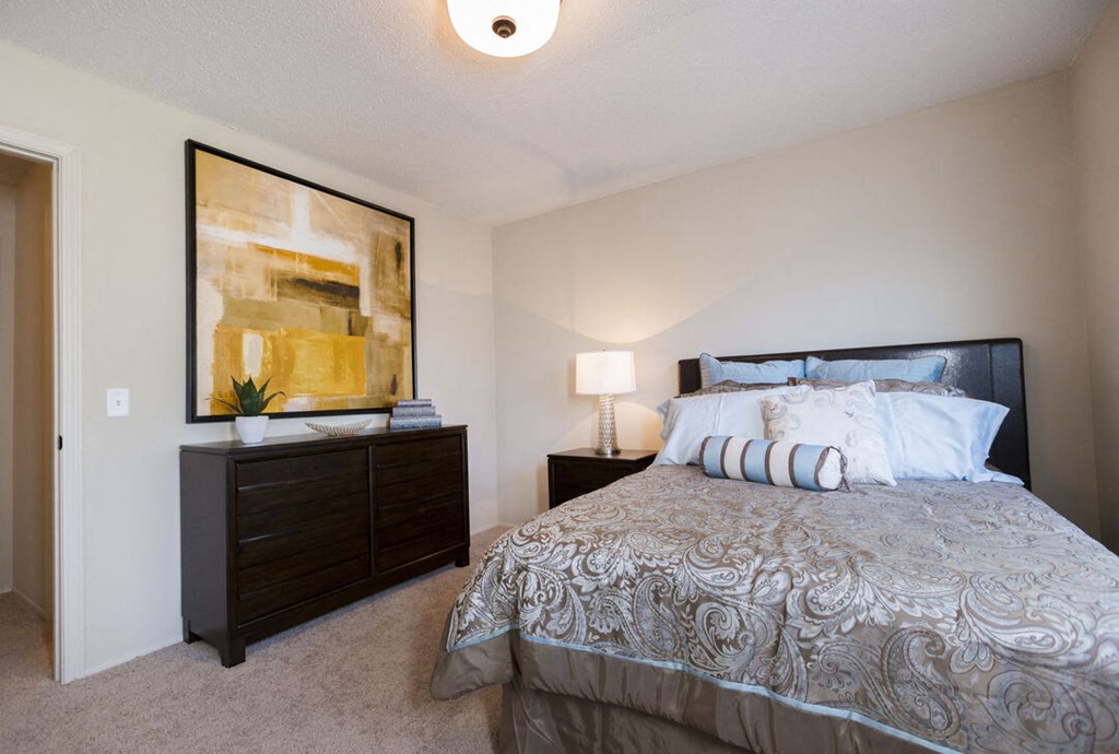 A bedroom with a bed, nightstand, and a painting on the wall.