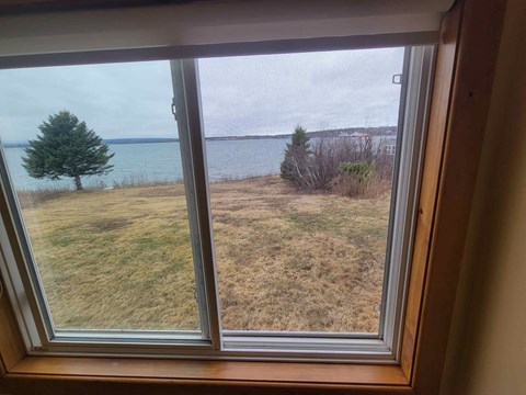 A view from a window looking out to a grassy field and a body of water.