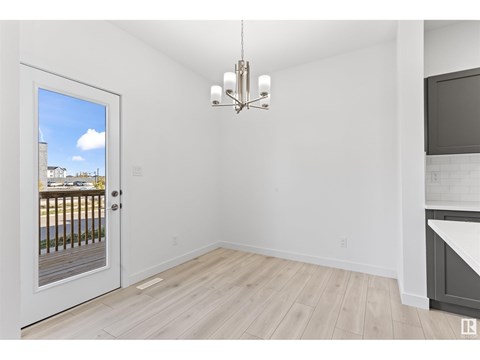 A room with a door leading to a balcony, a chandelier, and a kitchen area with a countertop and cabinets.
