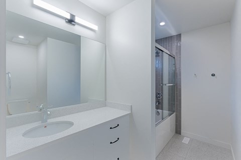 A white bathroom with a sink, mirror, and shower.