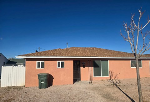 A house with a brown roof and a green trash bin in front.