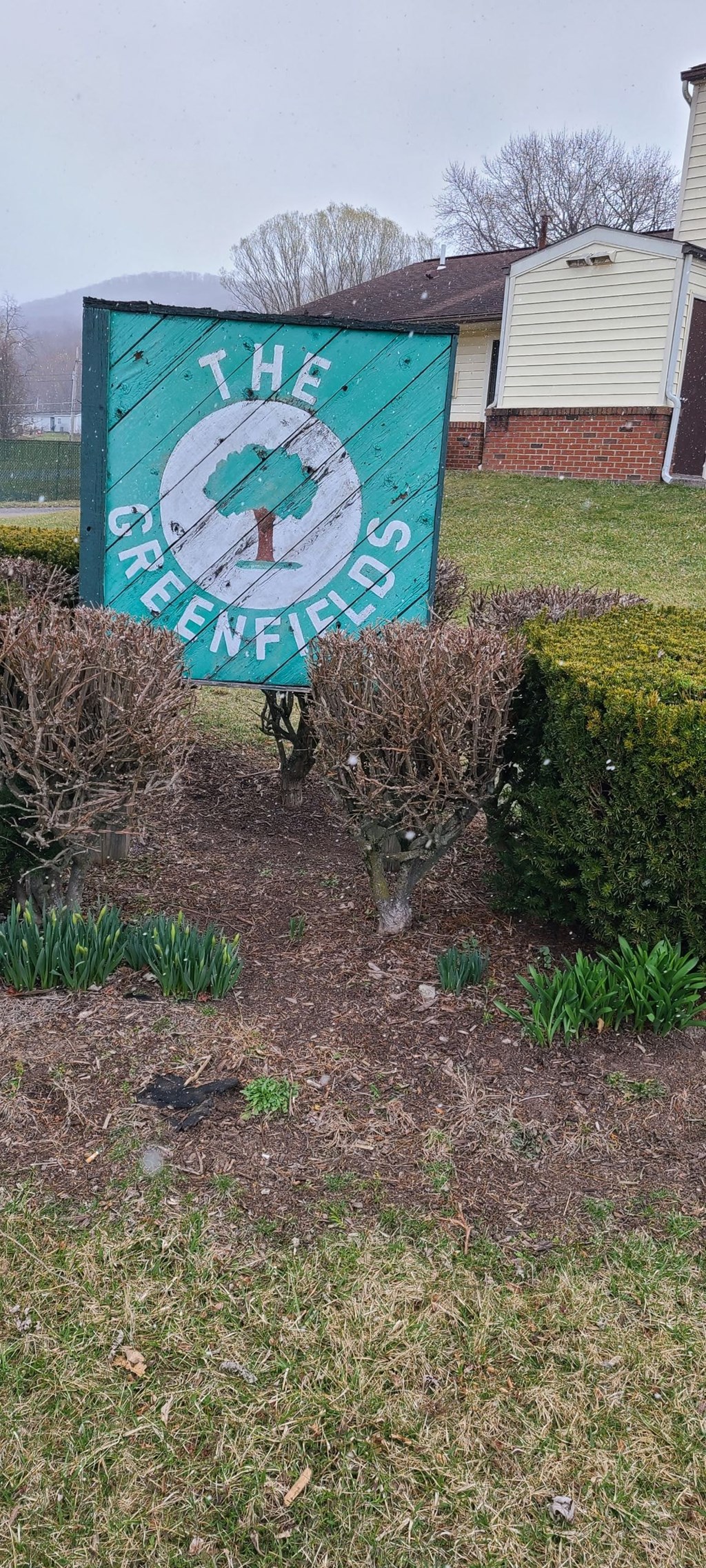A sign that says "The Greenfields" is in front of a house.