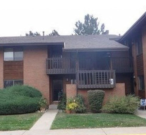 A brick building with a balcony and bushes in front.