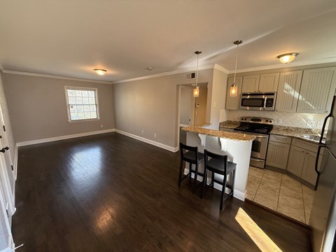 A kitchen with a countertop and chairs is visible.