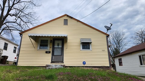 A yellow house with a blue sign in front.