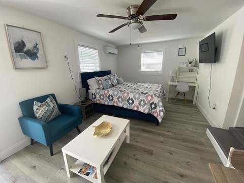 A bedroom with a bed, a blue chair, a white table, and a ceiling fan.