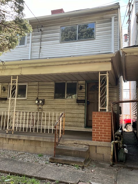 A house with a grey siding and a red brick pillar.