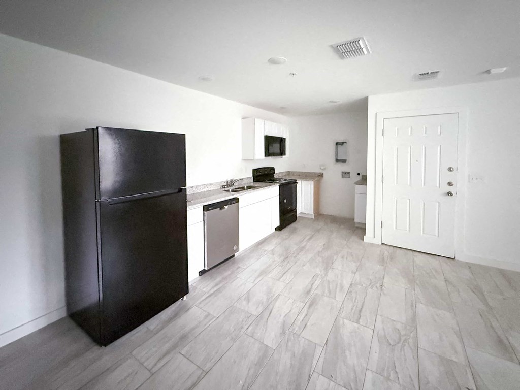 A kitchen with a black fridge, microwave, dishwasher and a white door.