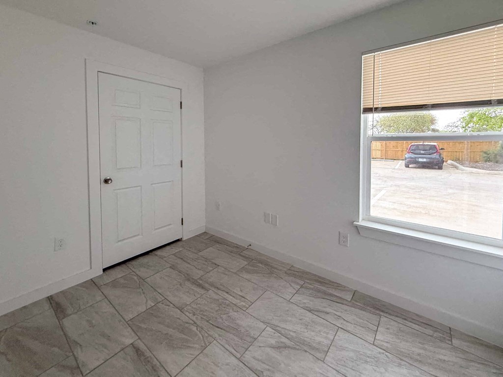 A room with a white door and a window showing a parking lot outside.