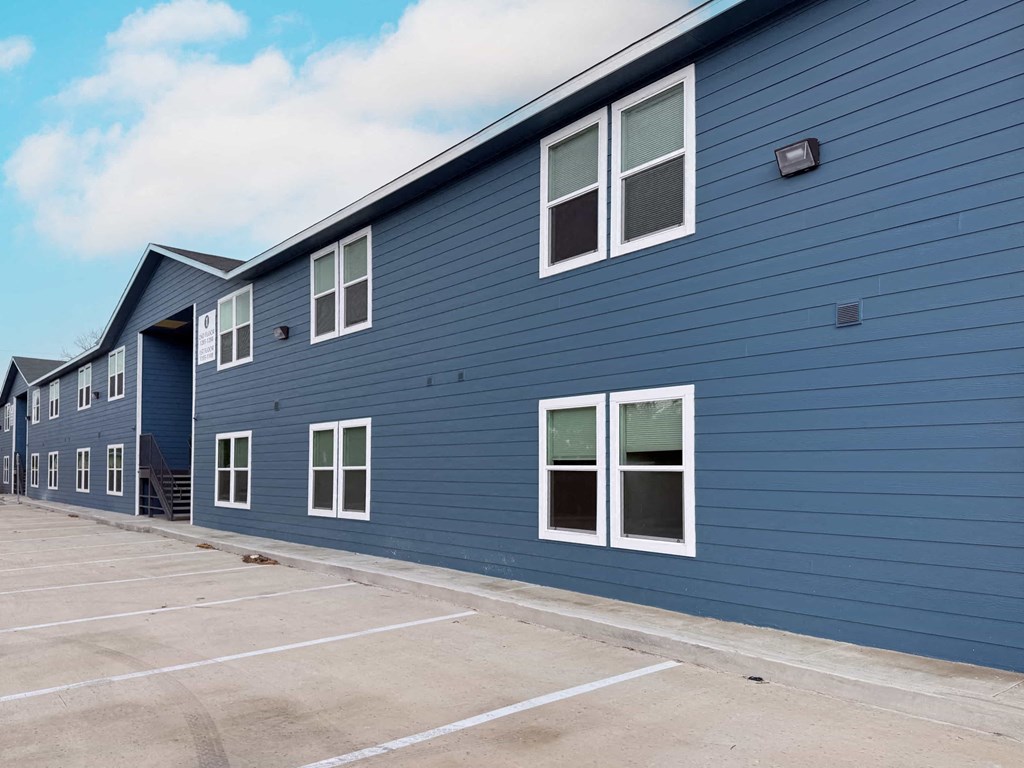 A blue building with white windows and a parking lot in front.
