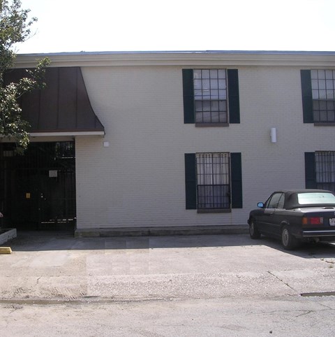 A black car is parked in front of a white building with black shutters.