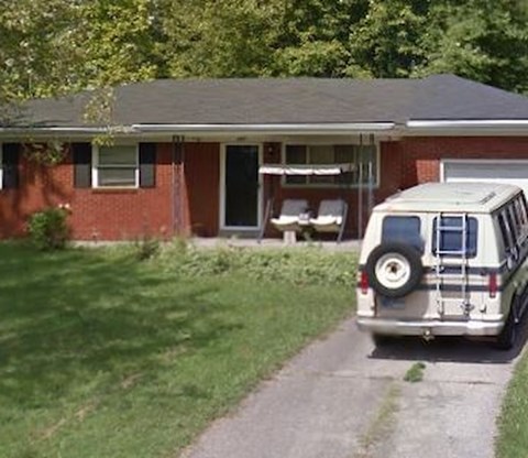 A white van is parked on a driveway in front of a red brick house.