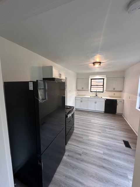 A black refrigerator in a kitchen with white cabinets.