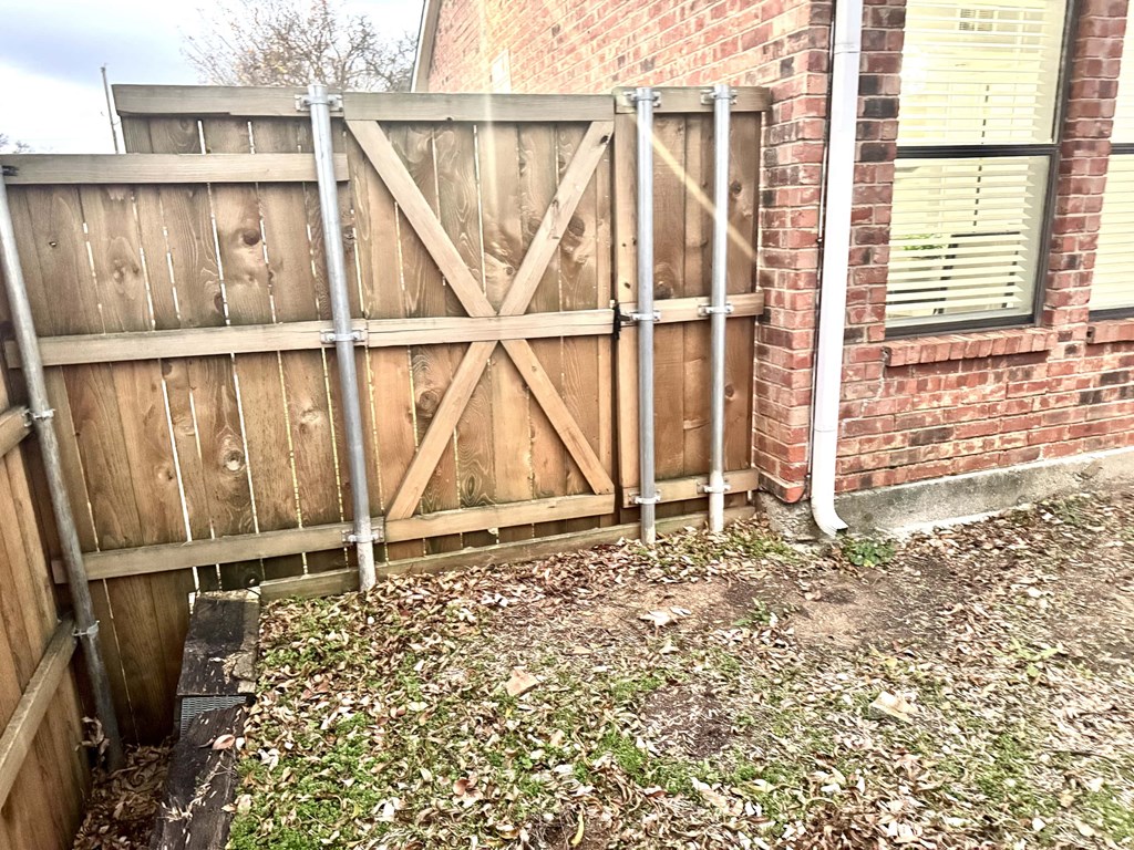 A wooden fence with metal posts is in front of a brick building.