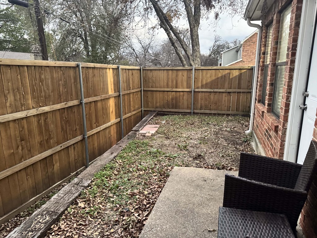 A backyard with a wooden fence and a brick building in the background.