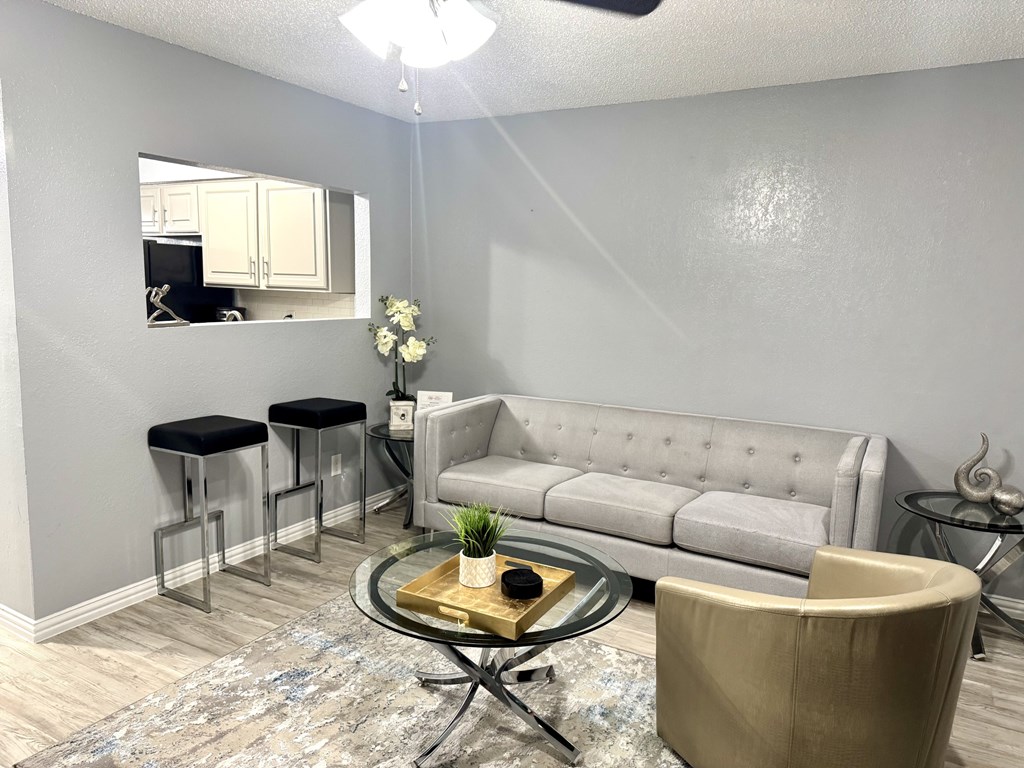 A living room with a grey couch, a glass coffee table, and a mirror on the wall.