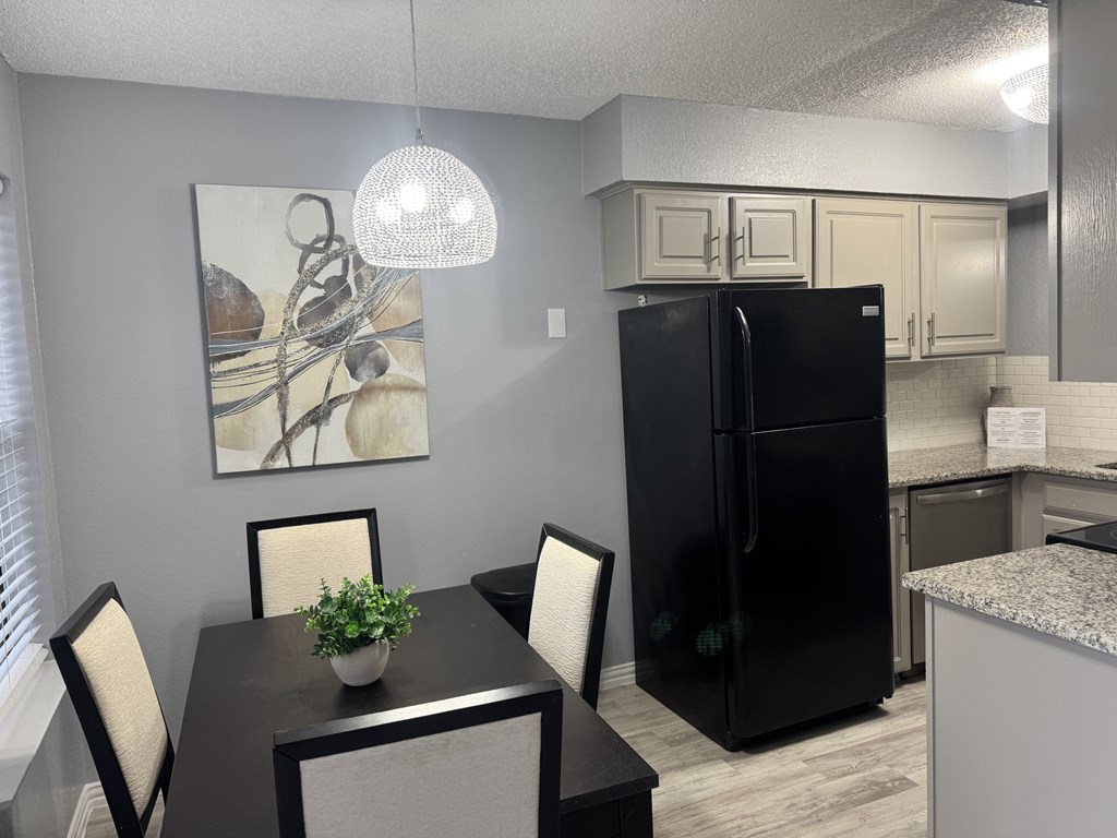 A black refrigerator is in a kitchen with a table and chairs.
