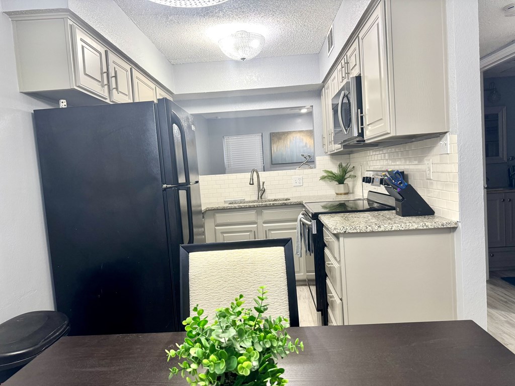 A black refrigerator is in a kitchen with white cabinets.