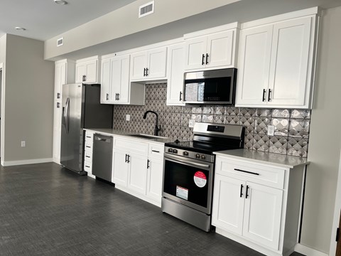 A kitchen with white cabinets and a black backsplash.